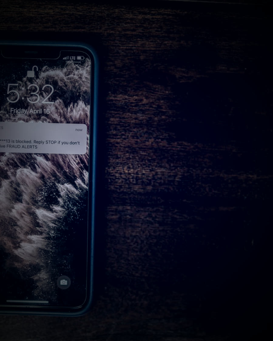 Celular exibindo alerta de bloqueio por fraude sobre mesa de madeira